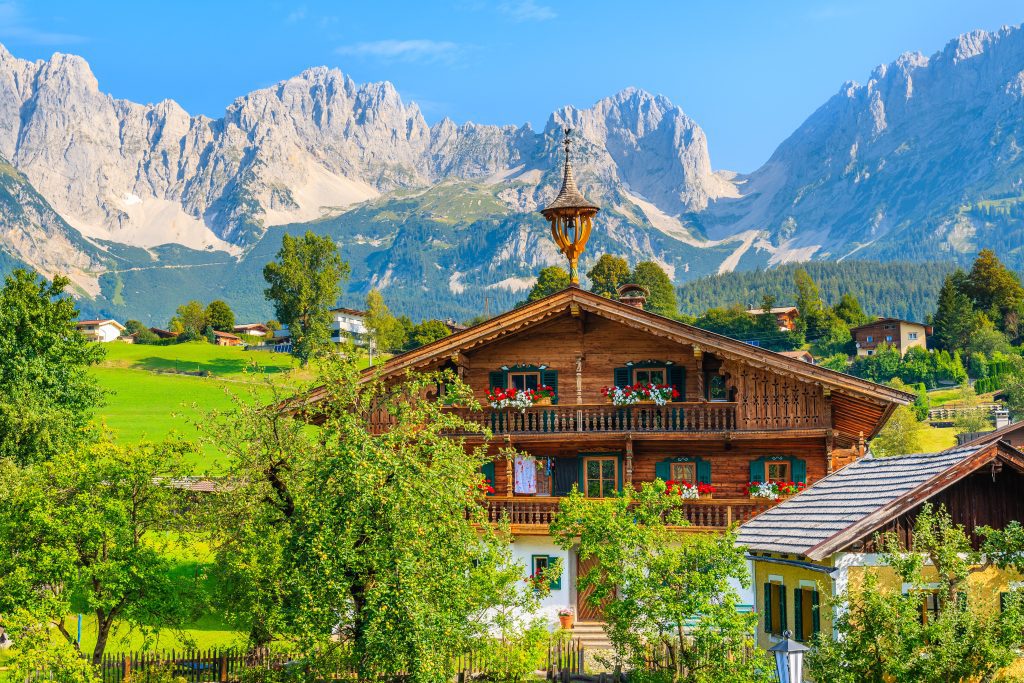 Typical wooden alpine house against Alps mountains background on green meadow in Going am Wilden Kaiser village on sunny summer day, Tyrol, Austria