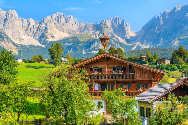Maison alpine typique en bois sur fond de montagnes des Alpes dans une prairie verte dans le village de Going am Wilden Kaiser par une journée d'été ensoleillée, Tyrol, Autriche.